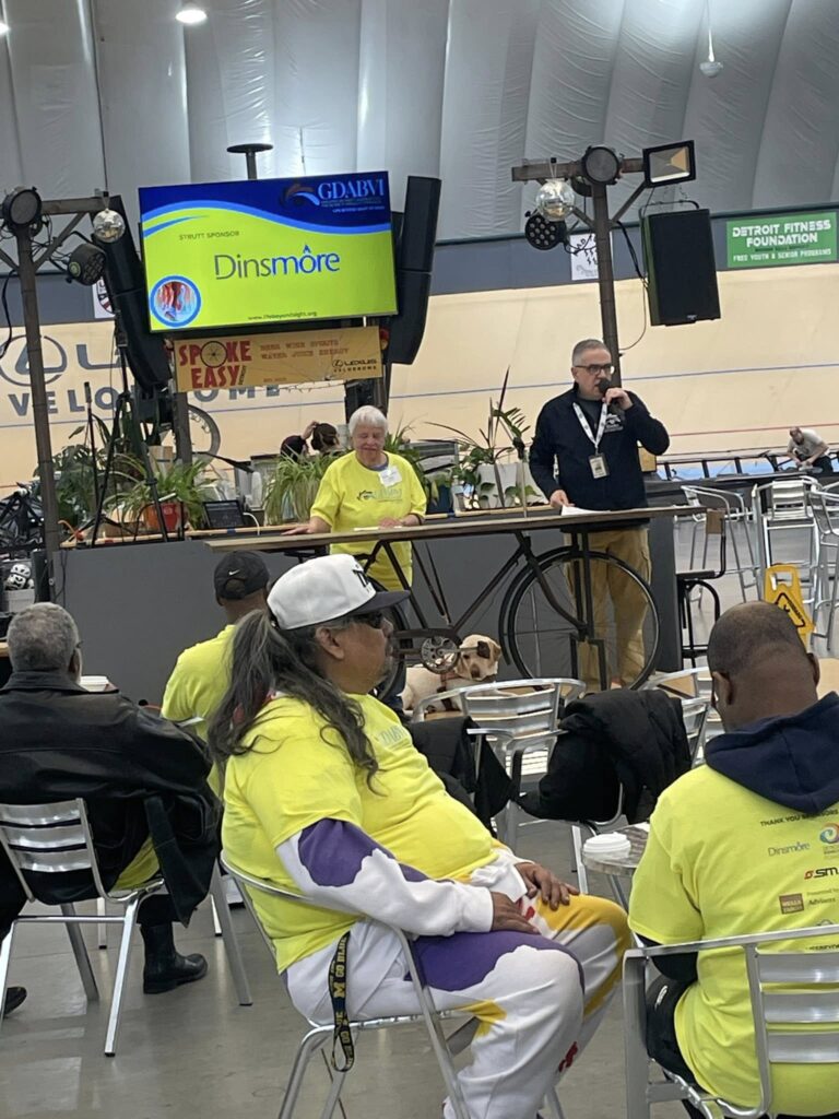 GDABVI board president, Cathy McAdam, onstage while GDABVI Executive Director, Jim Smock, speaks at the GDABIV 5K Walk.