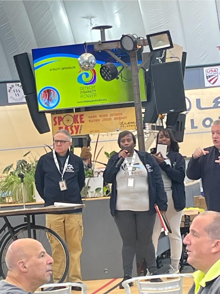 Multiple people on stage while GDABVI's Kashonia Graham speaks at the GDABIV 5K Walk.